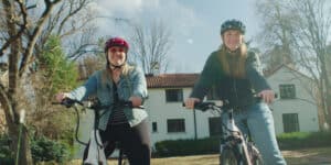 Two young women riding ebikes through a neighborhood.